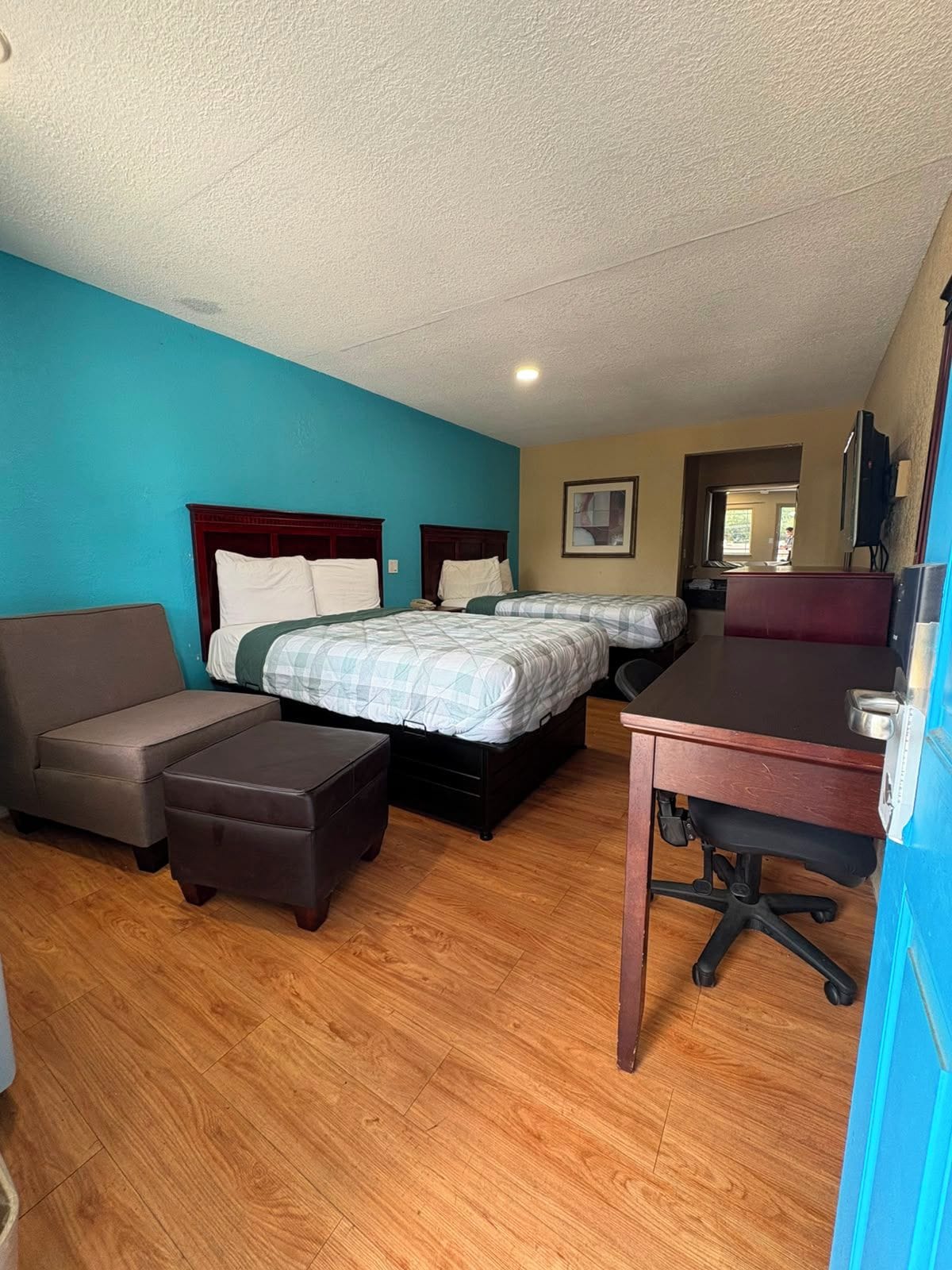 A hotel room with two beds, a desk, a chair, and a sofa.