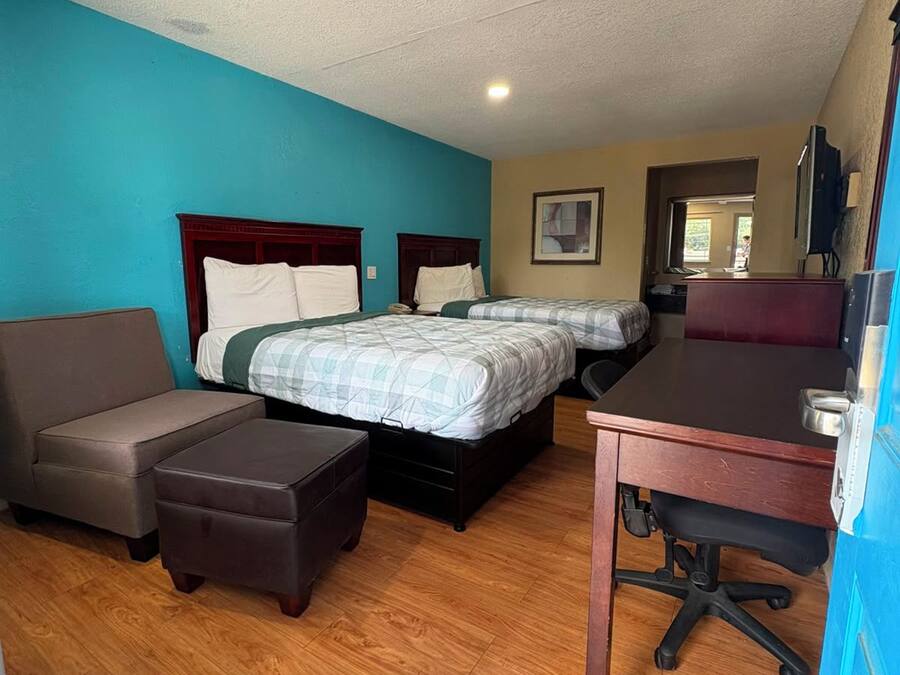 Quarto de hotel com duas camas, uma escrivaninha, uma cadeira e um sofá.