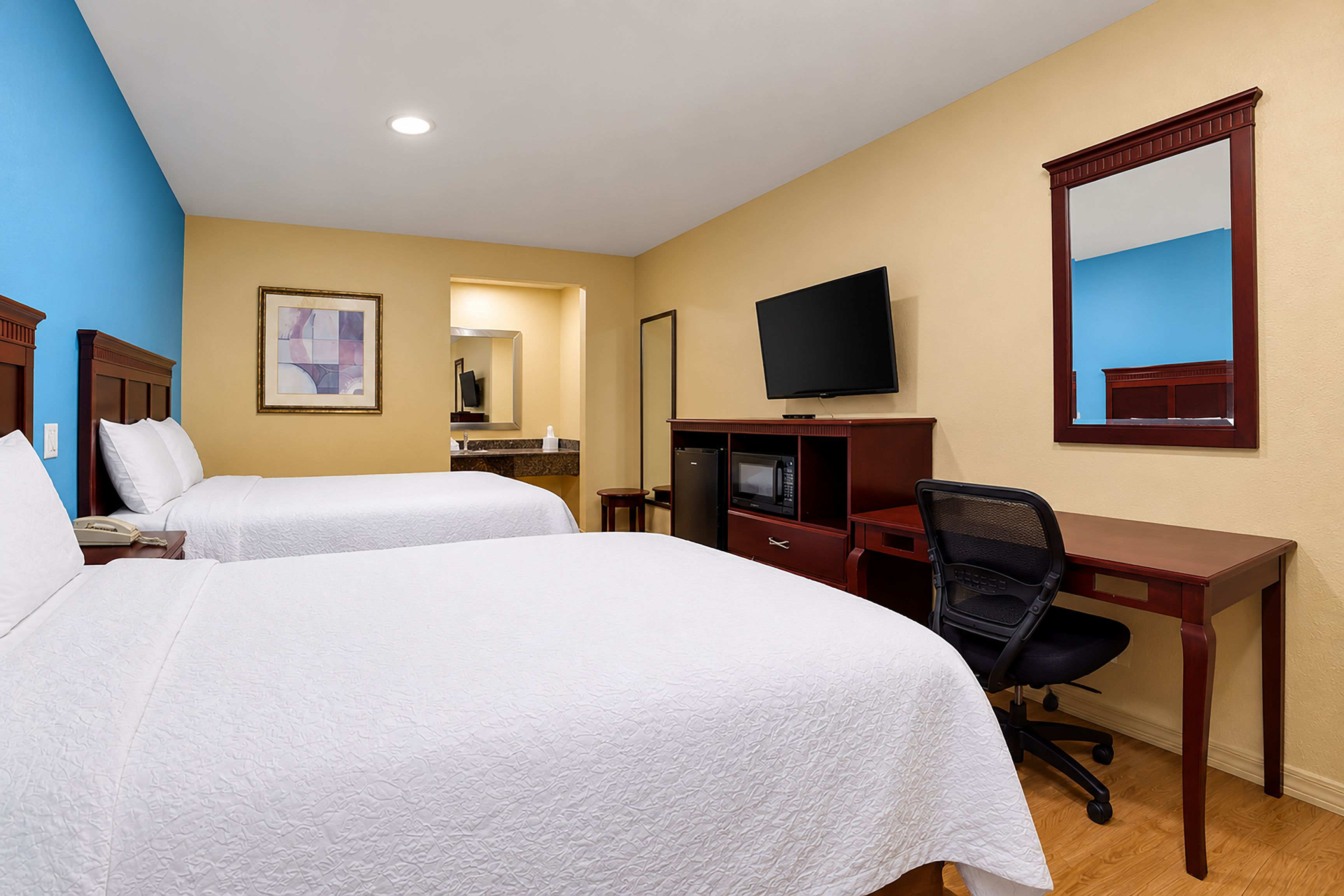 Habitación de hotel con dos camas, un escritorio, una silla, un televisor y un espejo.