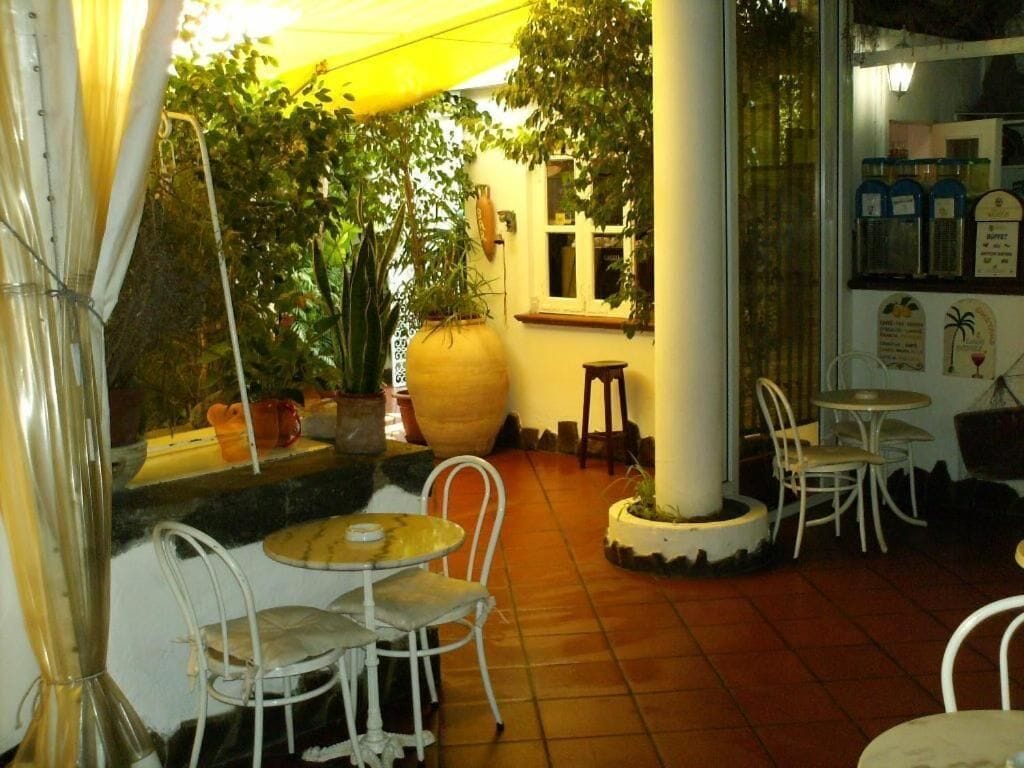 Un patio al aire libre con sillas y mesas de metal blanco, rodeado de plantas en macetas y una jardinera grande.