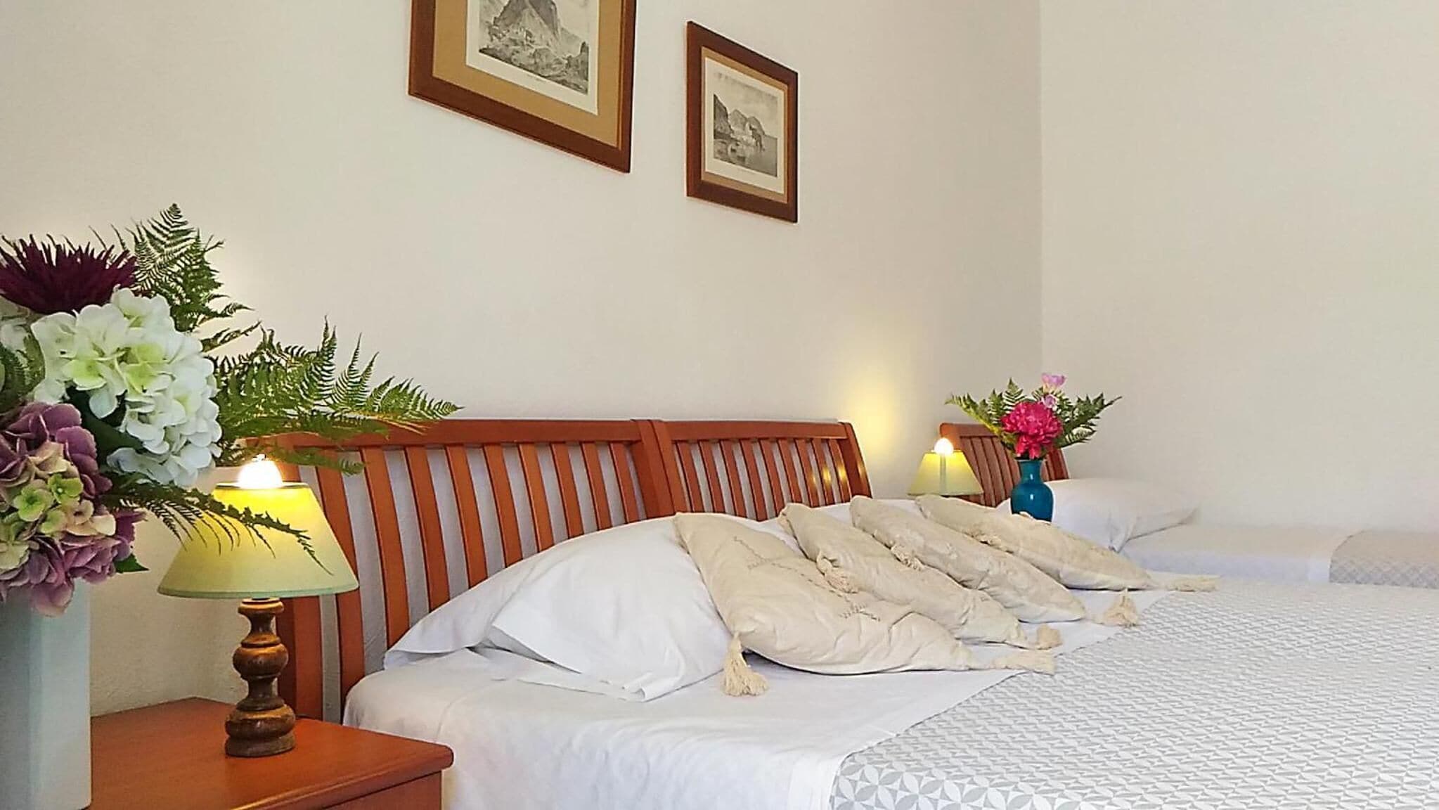 A hotel room with a wooden headboard, two beds, a nightstand with a lamp, and two framed pictures on the wall.