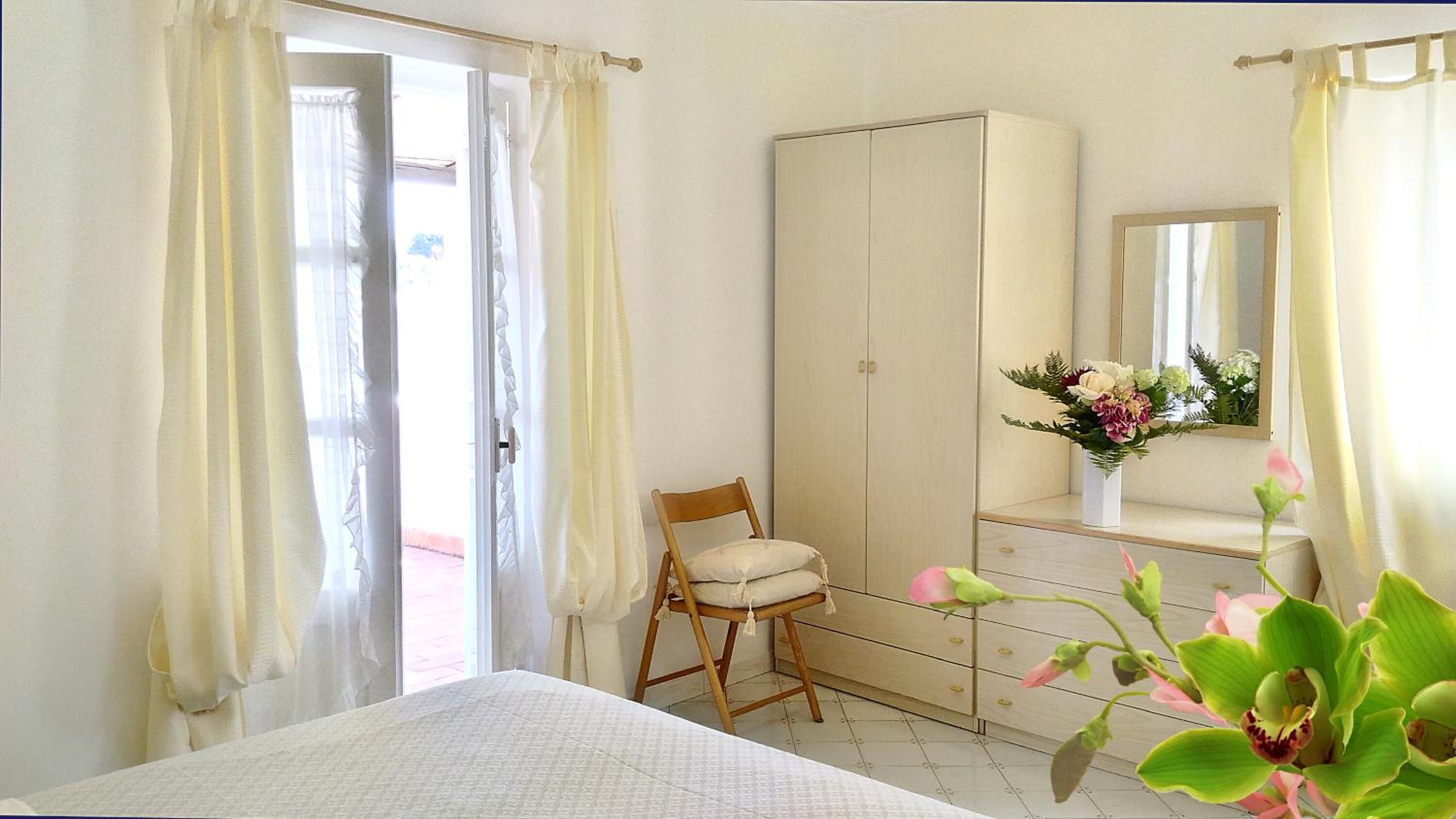 Quarto com cama, cadeira de madeira, guarda-roupa e espelho.