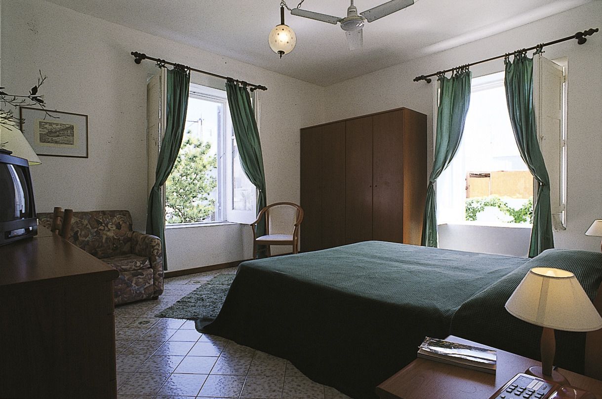 A bedroom with a bed, a chair, a desk, and a wardrobe.
