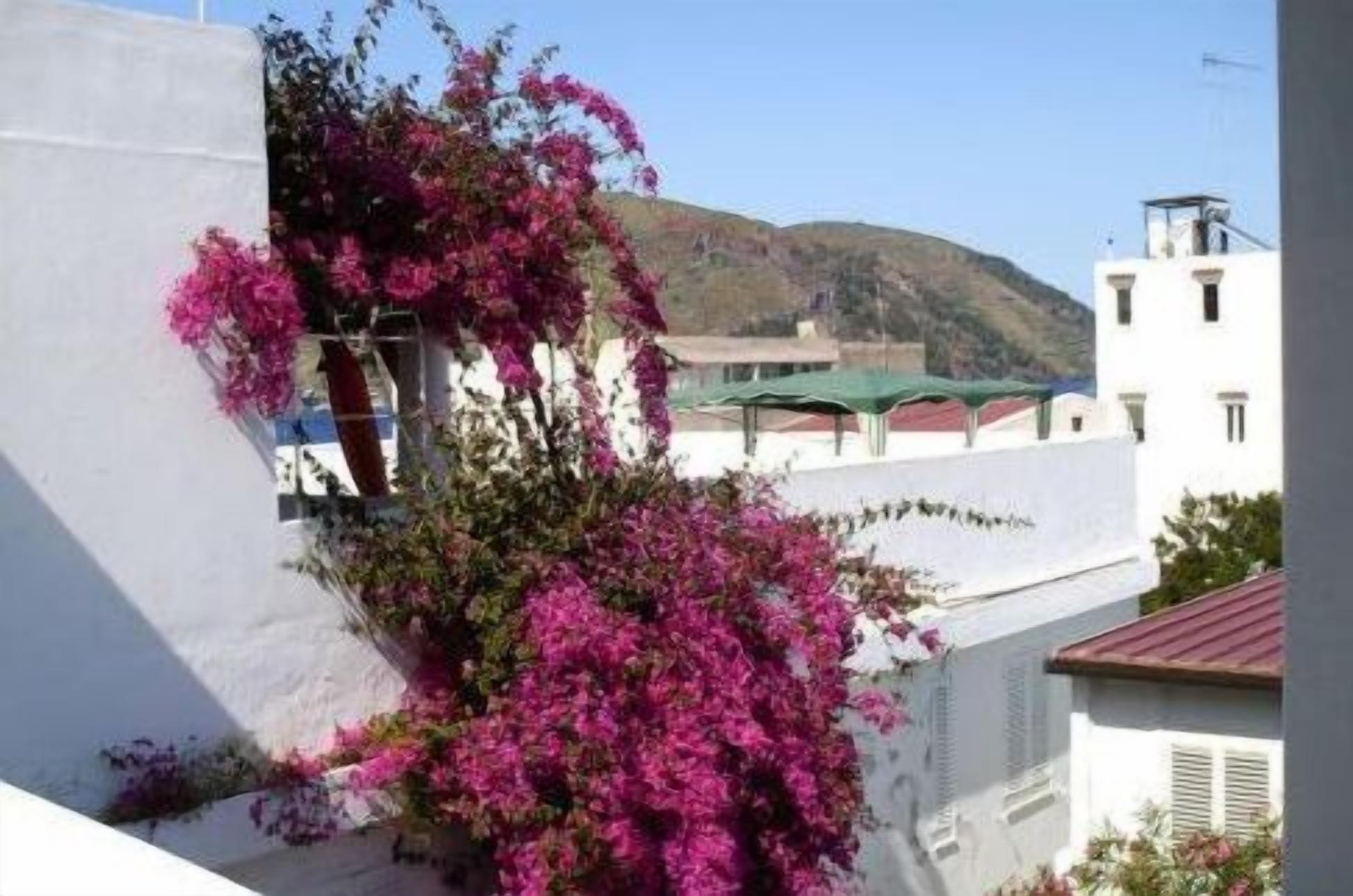 Un edificio bianco con un balcone e fiori di bouganvillea rosa.