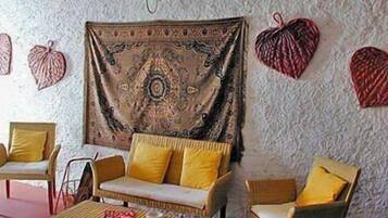 Una stanza accogliente con un divano, poltrone e un tavolino. Un arazzo adorna la parete, e sono presenti oggetti decorativi.
