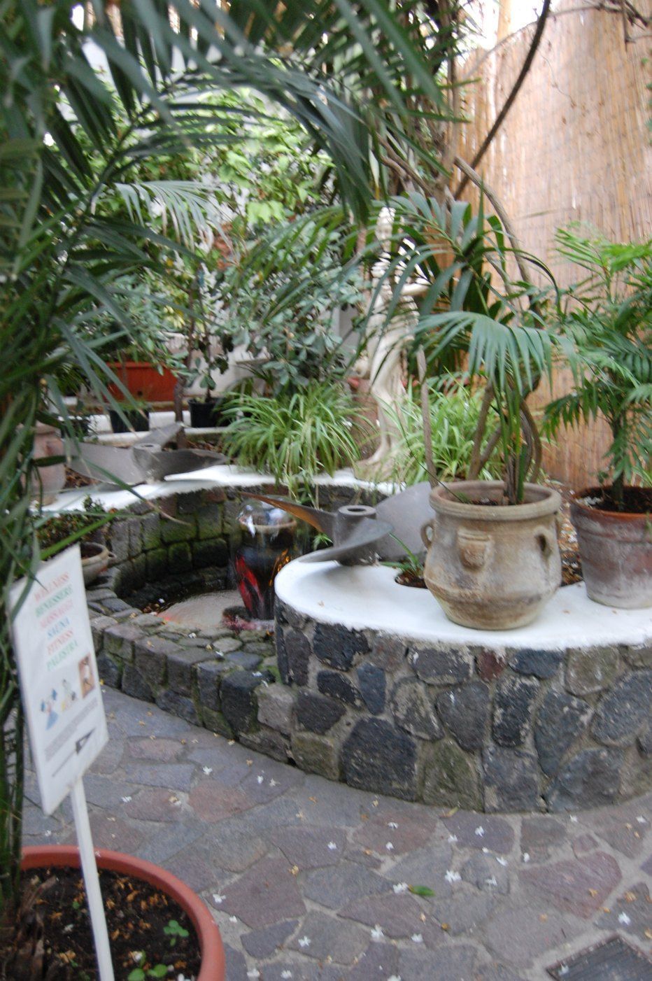 Una fuente de piedra rodeada de macetas con plantas y un letrero.