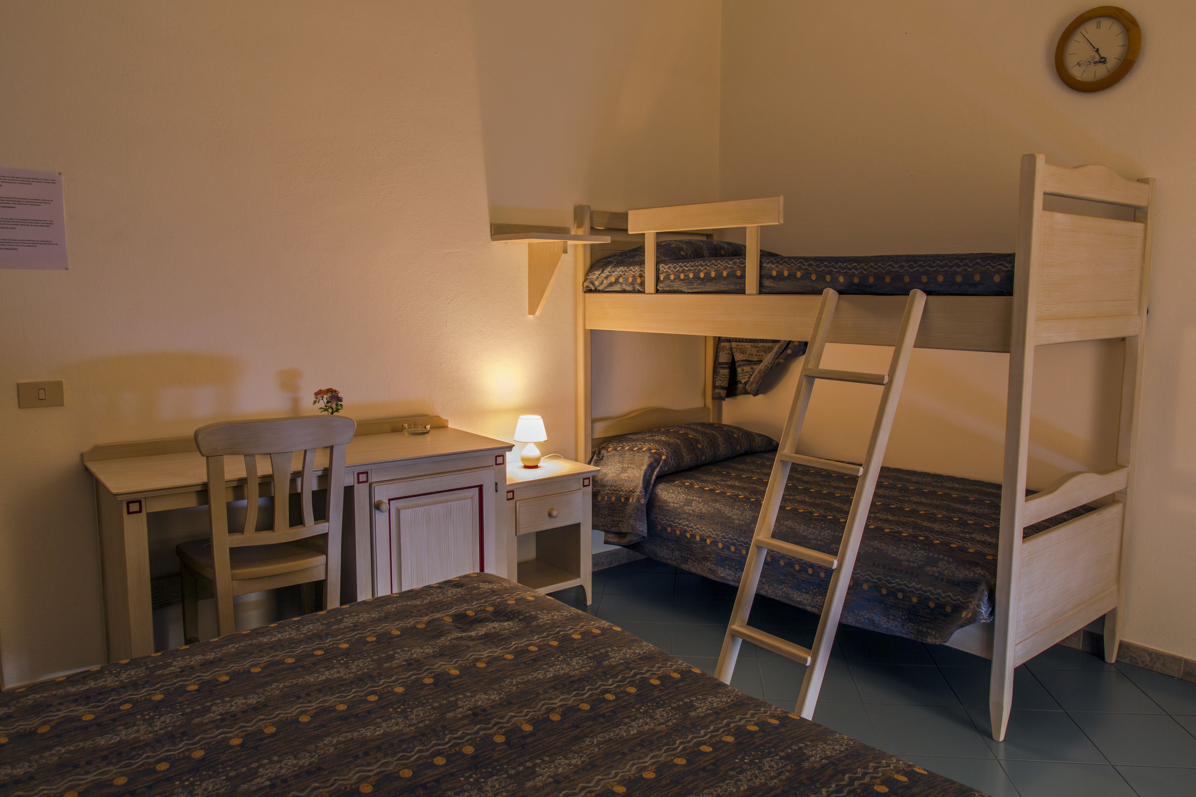 Un dormitorio con literas, un escritorio, una silla y una mesita de noche con lámpara.