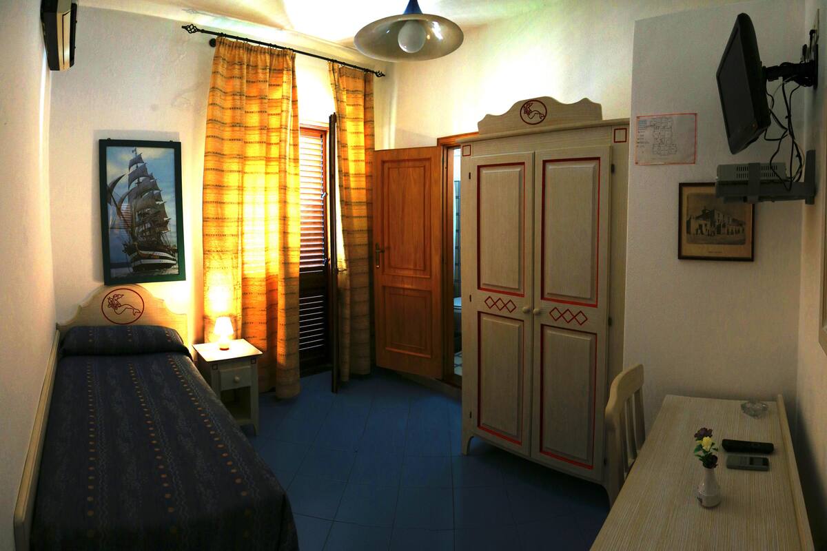 A bedroom with a bed, a nightstand with a lamp, a wardrobe, and a table with a vase.