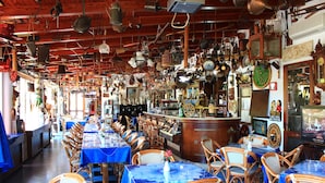 A restaurant with multiple tables and chairs, a bar area, and various kitchen utensils hanging from the ceiling. - Hotel Oriente (Lipari)