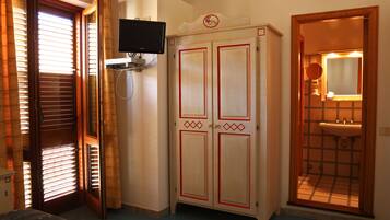 Une chambre comprenant un lit, une armoire, une télévision et une salle de bain avec un lavabo et un miroir.