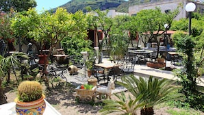An outdoor patio area with tables and chairs, surrounded by potted plants and a decorative horse-drawn carriage. - Hotel Oriente (Lipari)