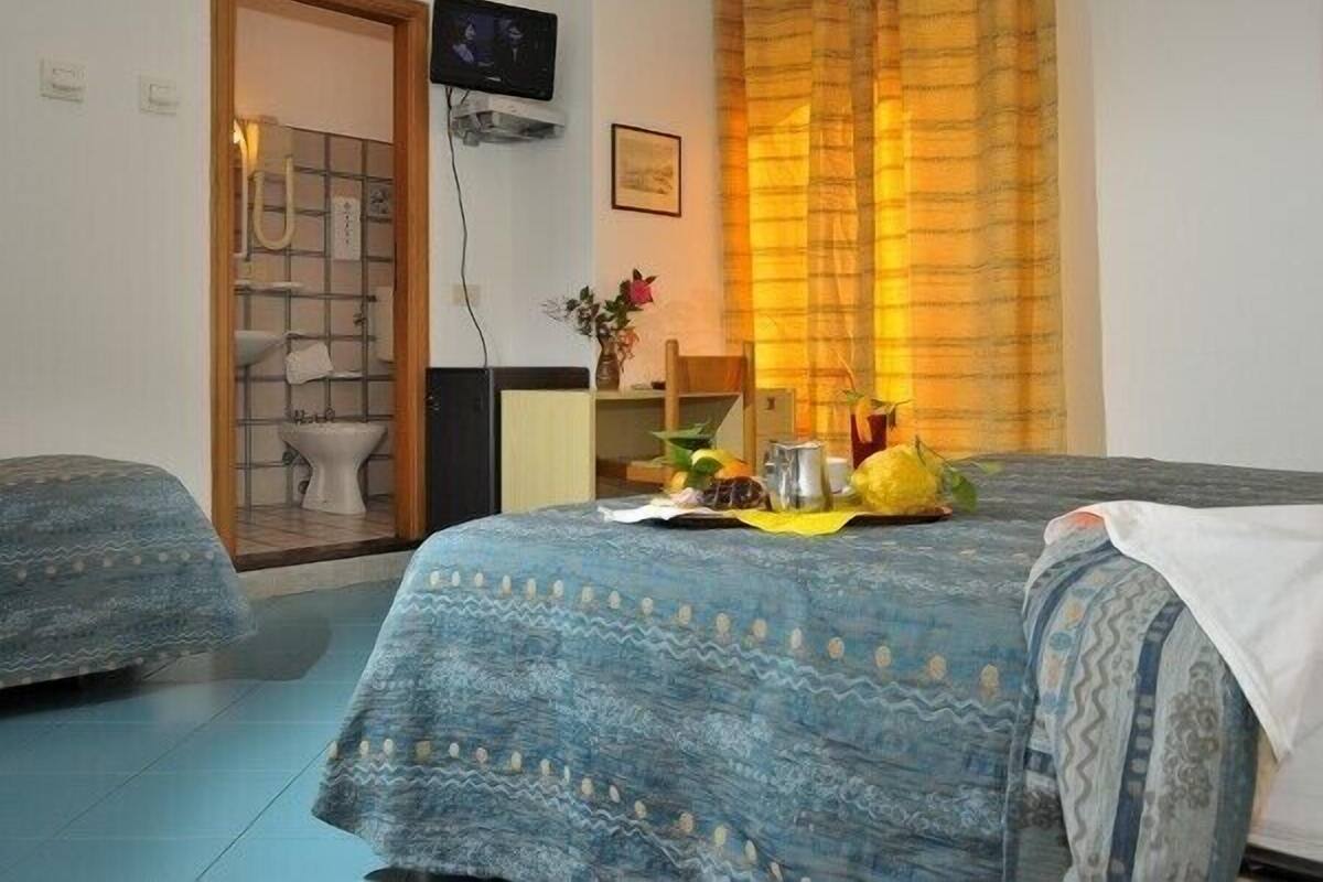 A hotel room with two beds, a television, a bathroom visible through an open door, and a small table with a vase of flowers.