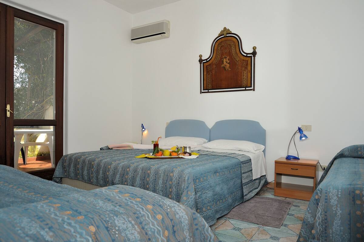 A bedroom with two beds, a wooden headboard, bedside tables, and a window with a view.