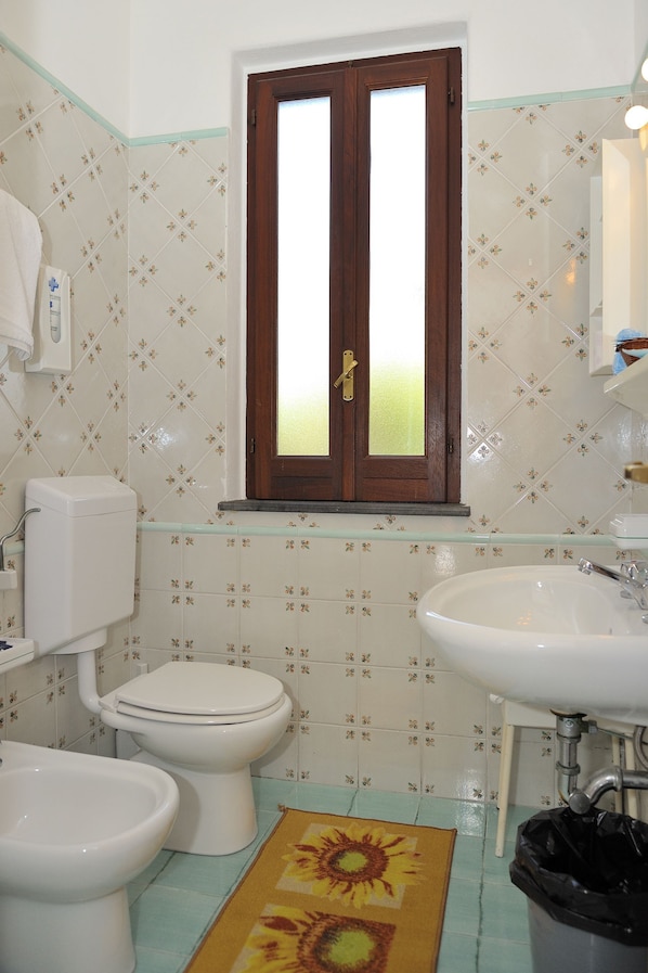 Un baño con inodoro, bidé, lavamanos y ventana con vista a la vegetación.