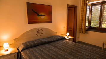 Una camera da letto con un letto, un comodino, una lampada, un quadro di un uccello, una finestra con tende e una porta.