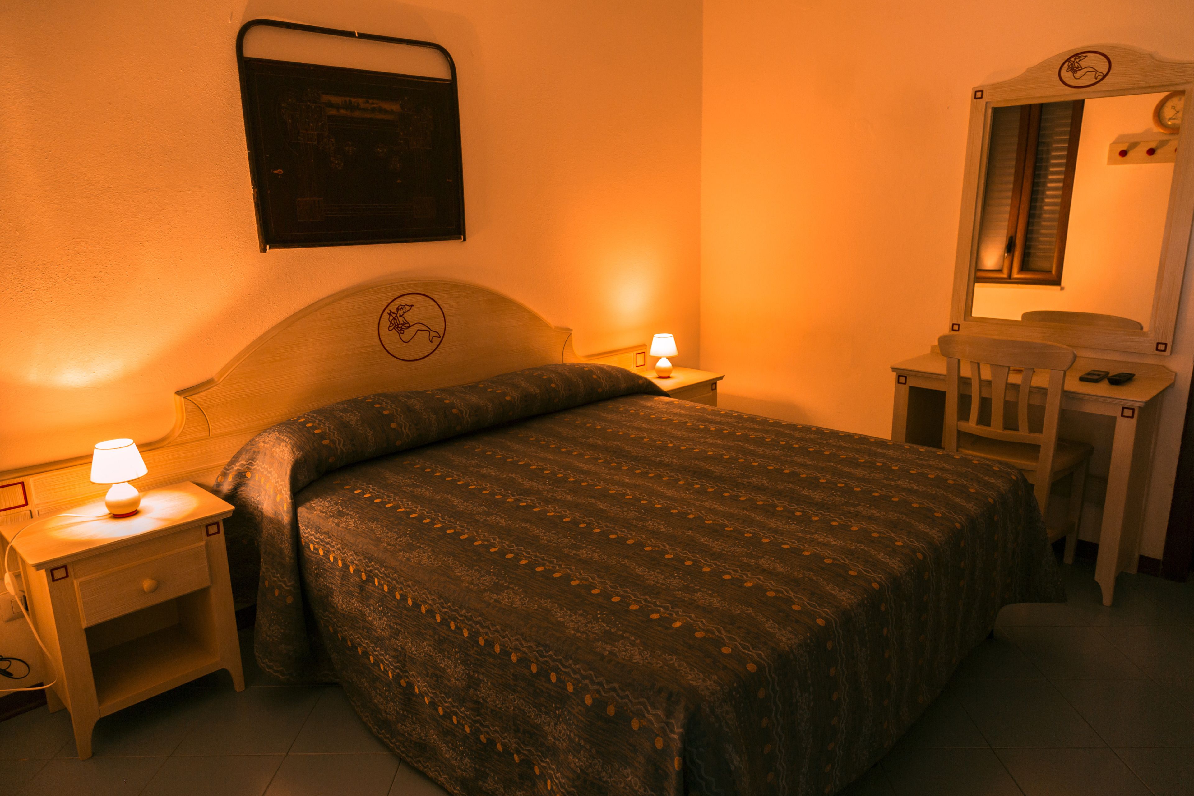 Un dormitorio con cama, mesitas de noche, un escritorio con silla y un espejo.