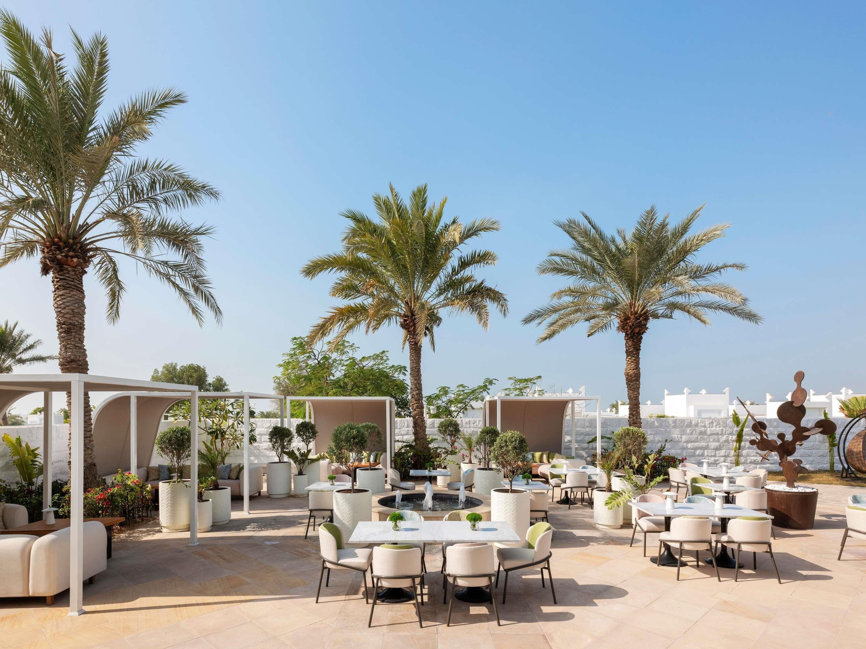 An outdoor patio area with round tables and chairs, palm trees, and potted plants.
