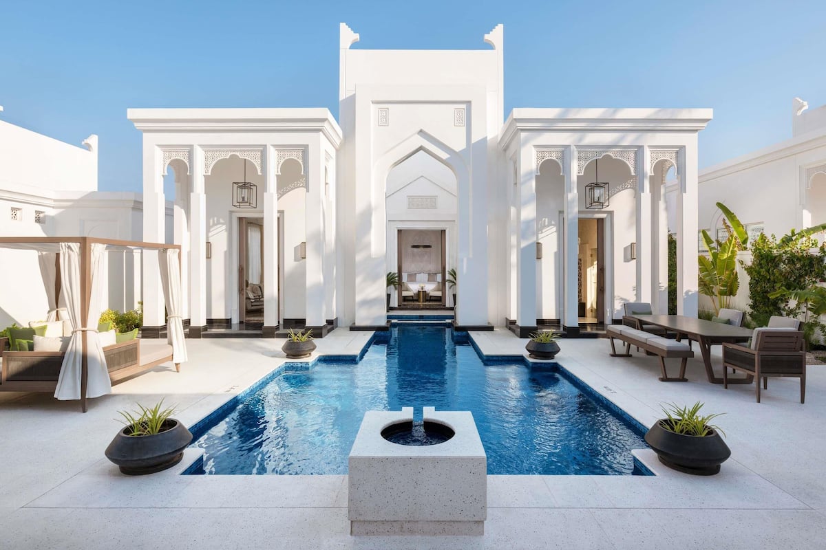 A pool area with a central pool, seating, and a building with arches and columns.