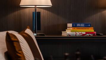 Une chambre d’hôtel bien rangée, avec une table de chevet sur laquelle se trouvent une lampe, une pile de livres et un jeu d’échecs.