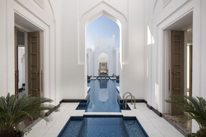 Zona de piscina con vista despejada a través de un arco, rodeada de paredes y puertas blancas.