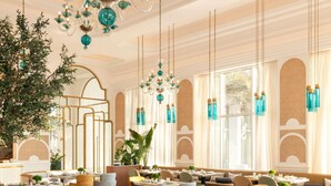Un vaste espace dédié à la salle à manger, avec de nombreuses tables et chaises, un grand lustre et de grandes fenêtres laissant entrer la lumière naturelle.