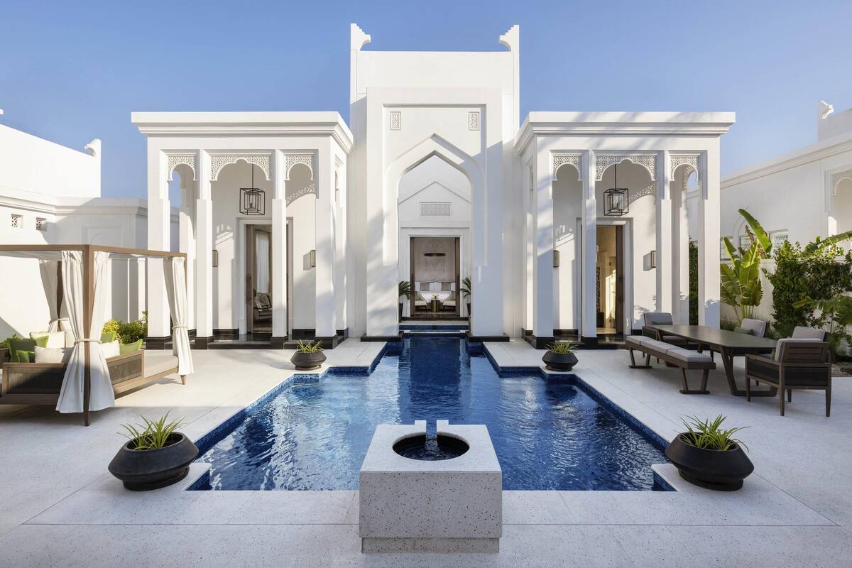 A pool with a fountain, surrounded by white buildings with arches and columns.