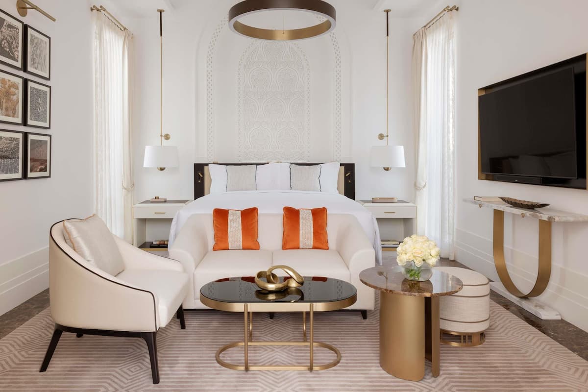 Una habitación de hotel moderna con una cama grande, un sofá, una mesa de centro, un televisor y un espejo decorativo.