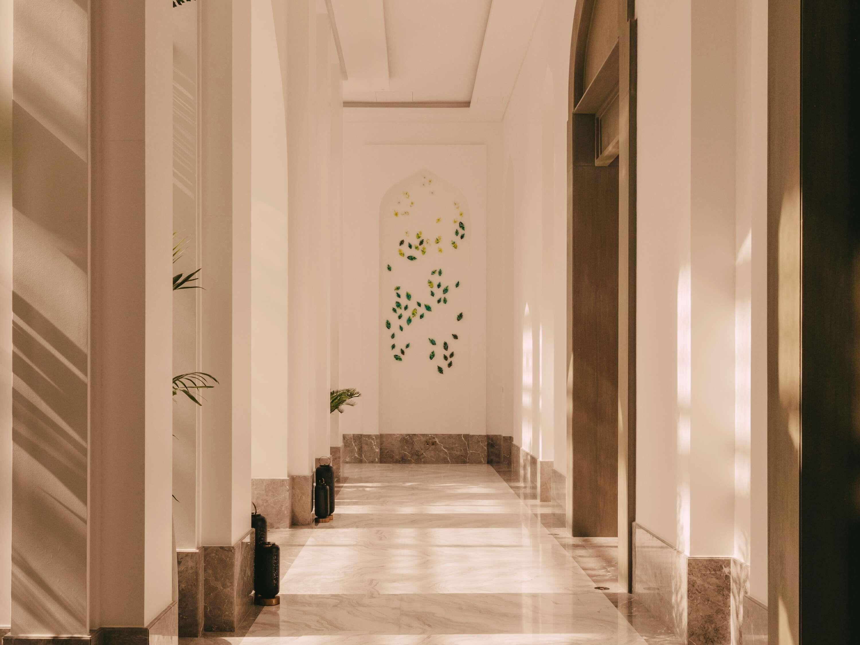A hallway with marble flooring, white walls, and a decorative wall art.