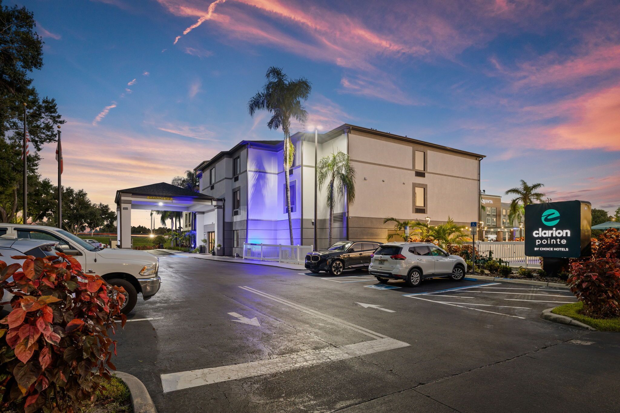 A hotel entrance with a modern design, including a blue-lit facade and a parking area with several cars.