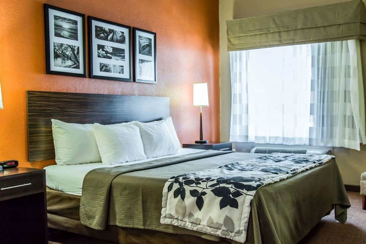 A hotel room with a bed, a nightstand, a lamp, and a window with curtains.