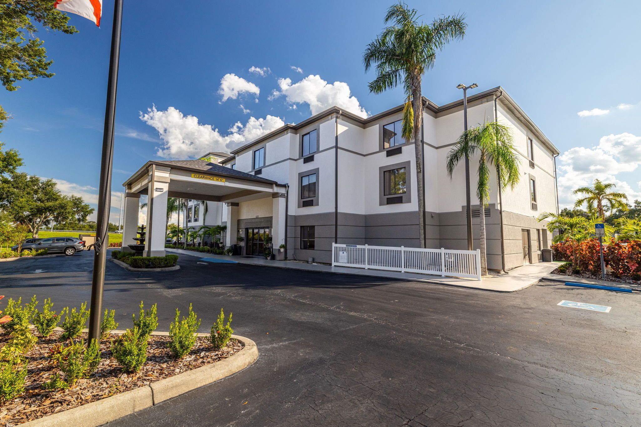 A modern hotel with a covered entrance, a parking lot, and a palm tree.