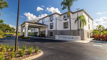 A modern hotel with a covered entrance, a parking lot, and a palm tree.