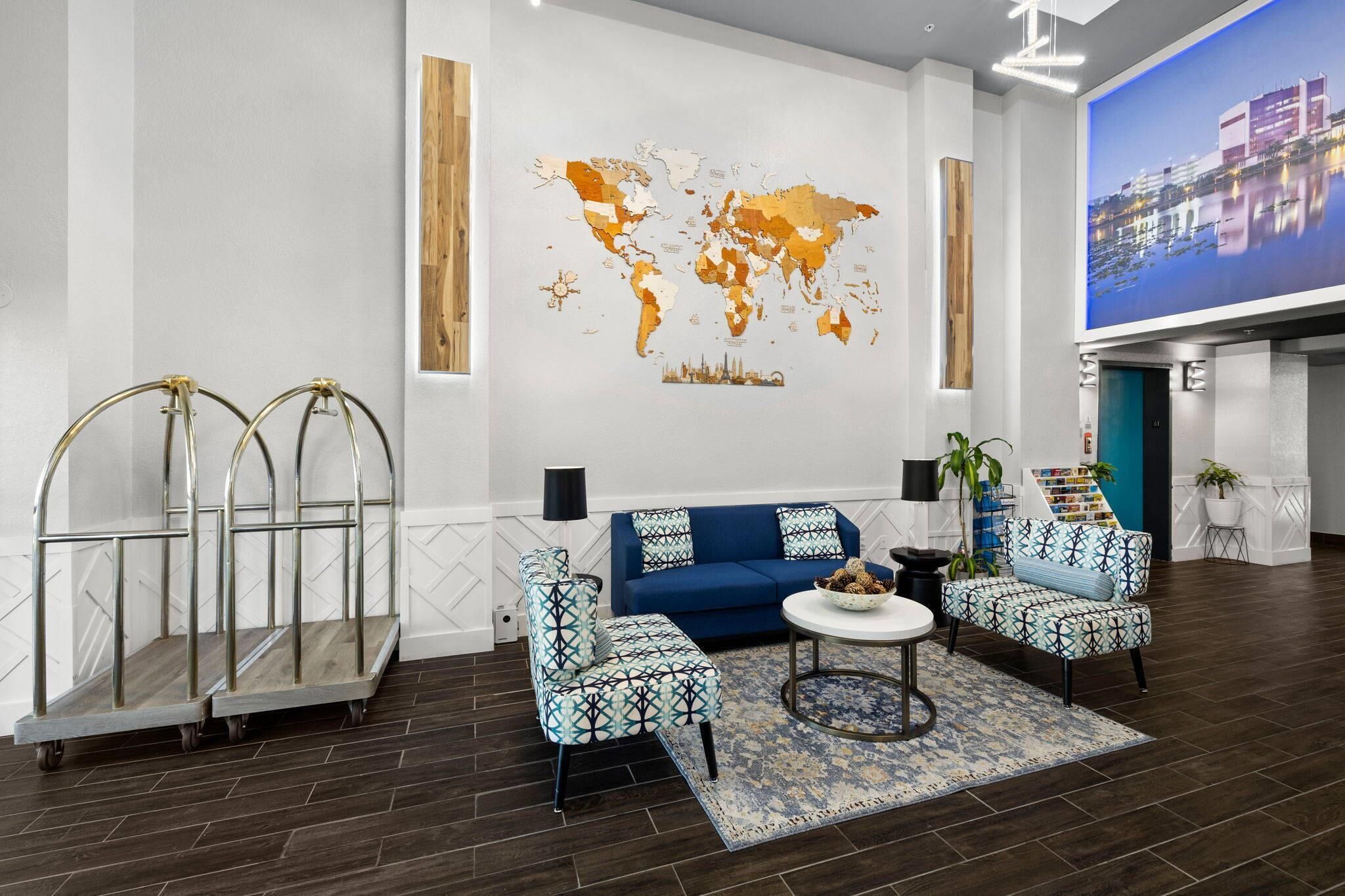 Un moderno hall de hotel con un mural de un mapa mundial, un conjunto de sofás azules y una pequeña mesa redonda.