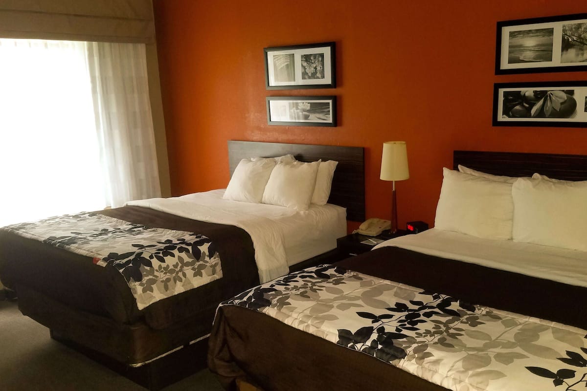 Two double beds with floral bedspreads, a nightstand with a lamp, and framed pictures on the wall.