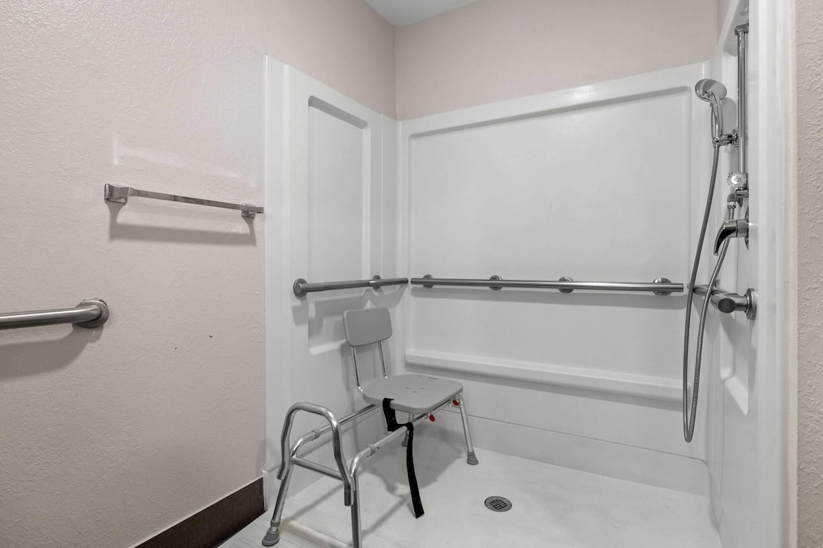 A bathroom with a white bathtub, a shower, a grab bar, and a wheelchair-accessible bench.