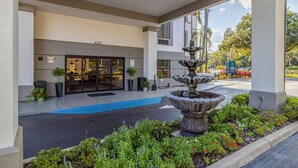 A hotel entrance with a fountain, potted plants, and a blue carpet leading to the door. - Clarion Pointe Lakeland I-4 (Lakeland)