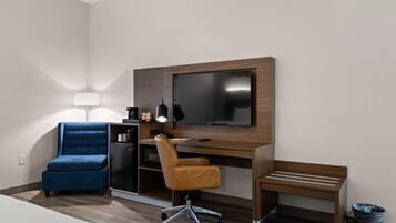 Una habitación de hotel moderna con una televisión de pantalla plana, un escritorio con una computadora, una silla azul, una silla marrón y un pequeño banco.