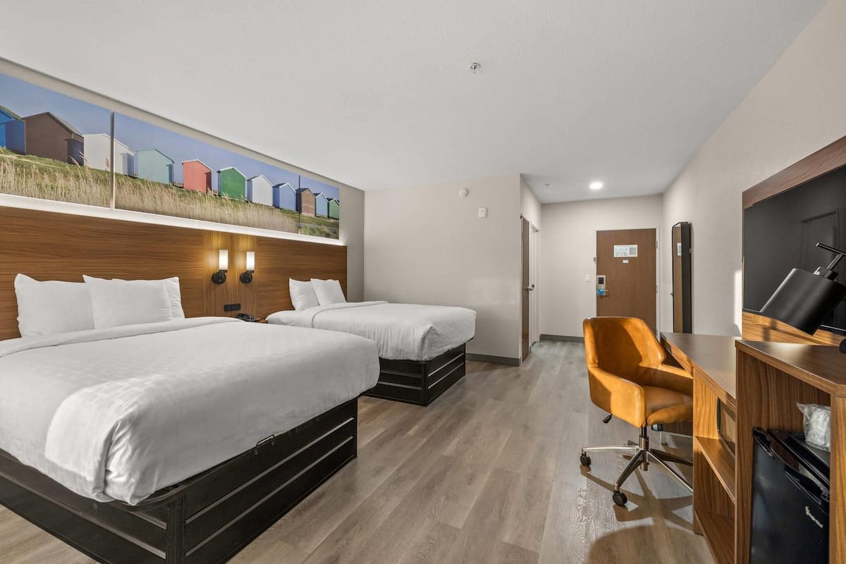 A hotel room with two beds, a desk, a chair, and a TV.