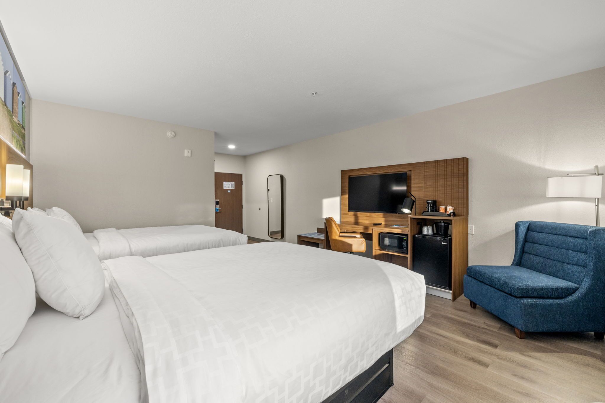 A hotel room with two beds, a desk with a chair, a TV, and a coffee machine.