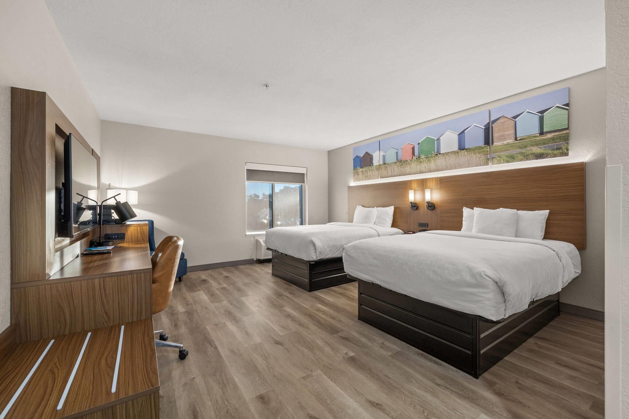 A hotel room with two beds, a desk with a computer, and a large window.