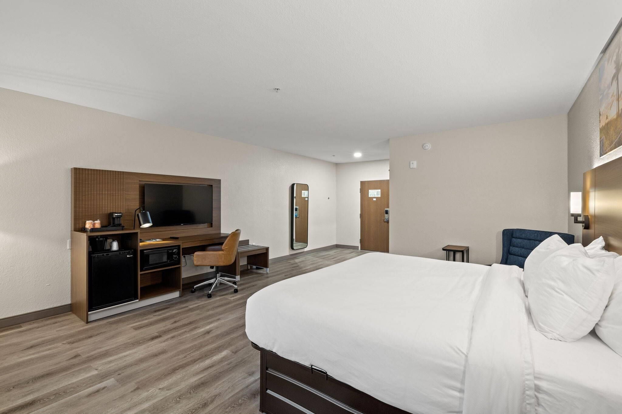 A hotel room with a bed, a desk with a chair, a television, and a small table.