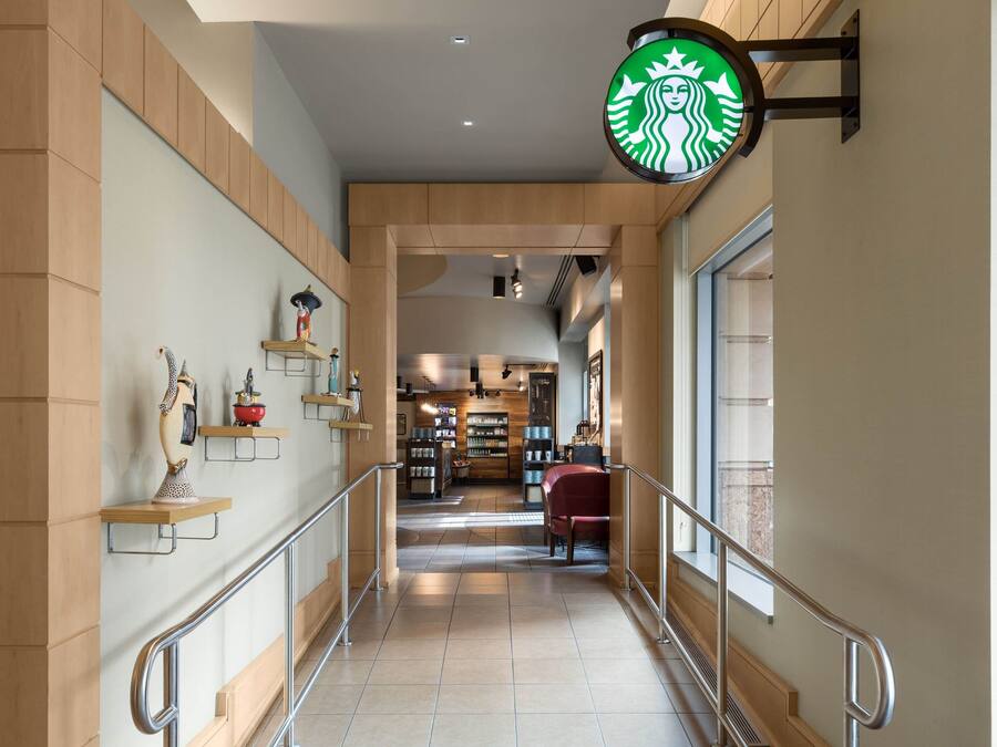 A hallway with a Starbucks sign, shelves with decorative items, and a seating area with a red chair.