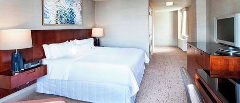 A hotel room with a large bed, a desk with a lamp, a television, and a painting on the wall.