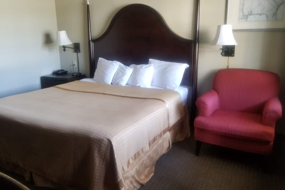 A hotel room with a large bed, a red armchair, and two bedside lamps.