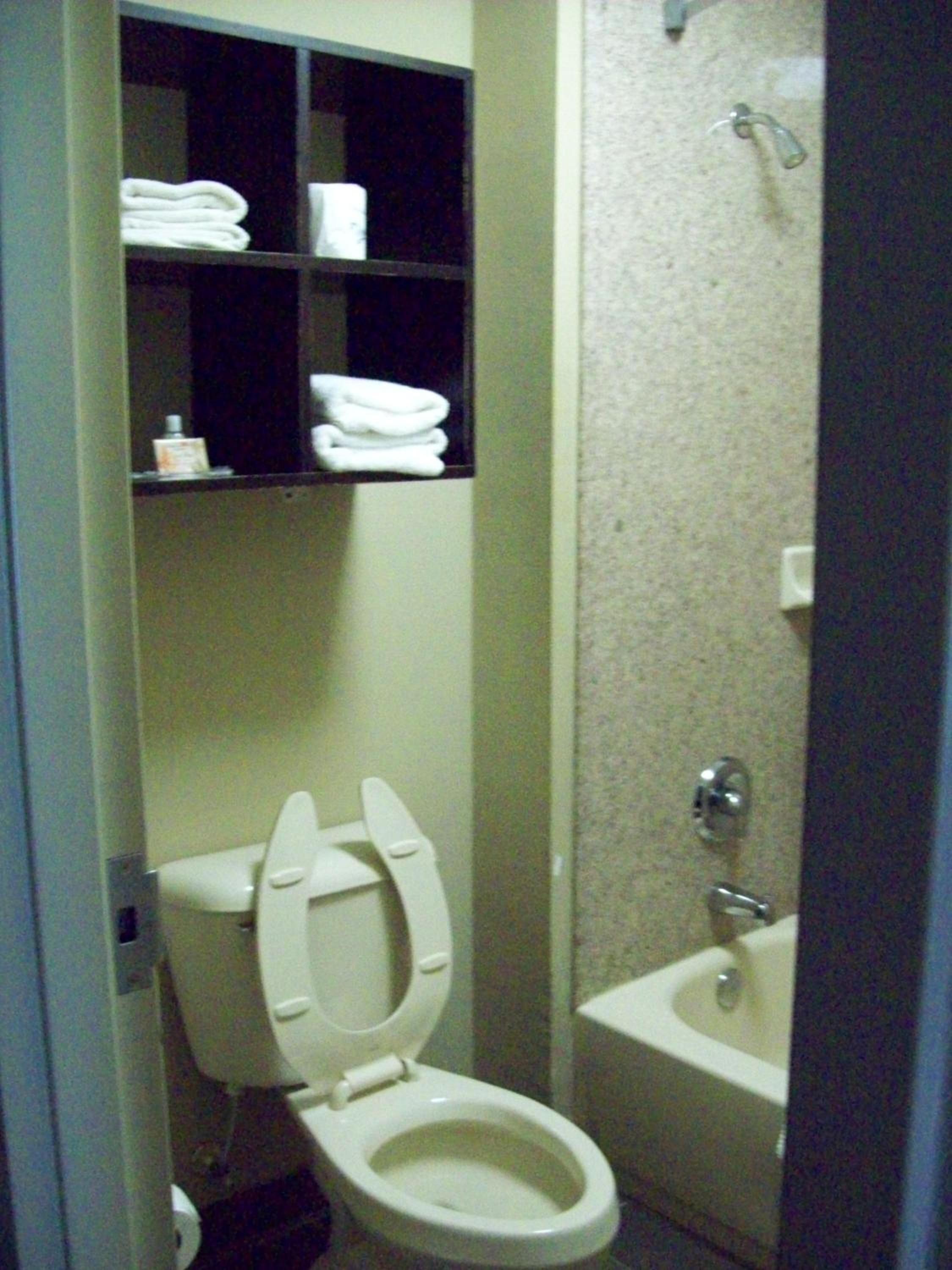 A bathroom with a toilet, a sink, and shelves above the toilet holding towels and toiletries.