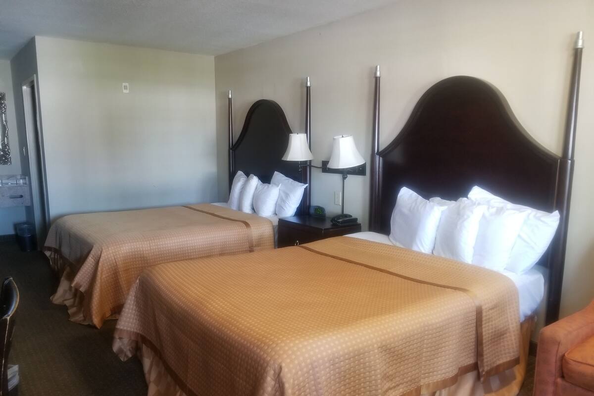 A hotel room with two beds, each with a headboard, a nightstand with a lamp, and a clock.