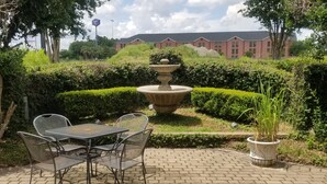 A patio area with a table and chairs, a stone fountain, and well-maintained hedges. - Inn at Mulberry Grove (Port Wentworth)