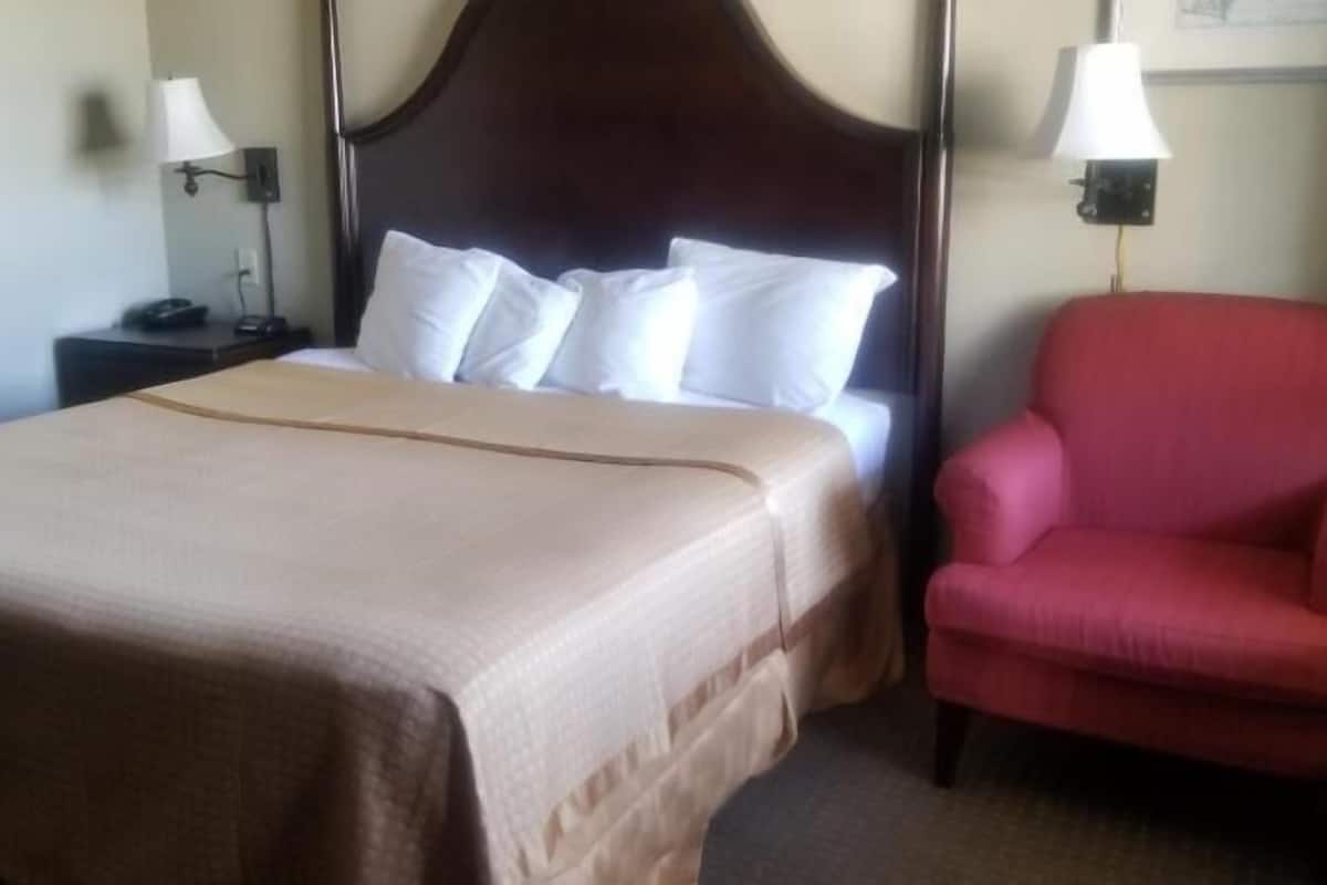 A hotel room with a bed, a nightstand, a red armchair, and two wall-mounted lamps.