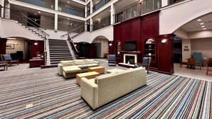 A spacious lobby with a central staircase, multiple balconies, a fireplace, and a seating area with sofas and chairs.