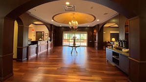A spacious lobby with a wooden floor, a central chandelier, and a reception desk.